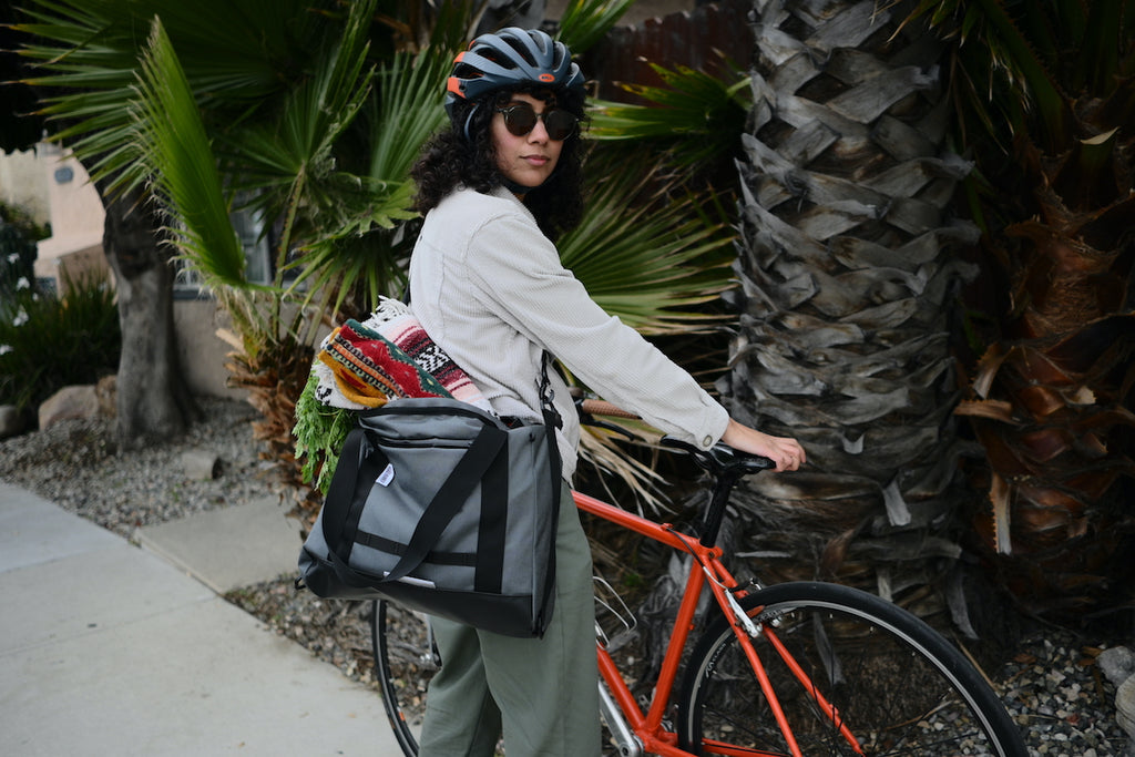 Woman with dark curly hair next to bike with a Road Runner Bags Everything Tote Bag filled with groceries, blanket and rug