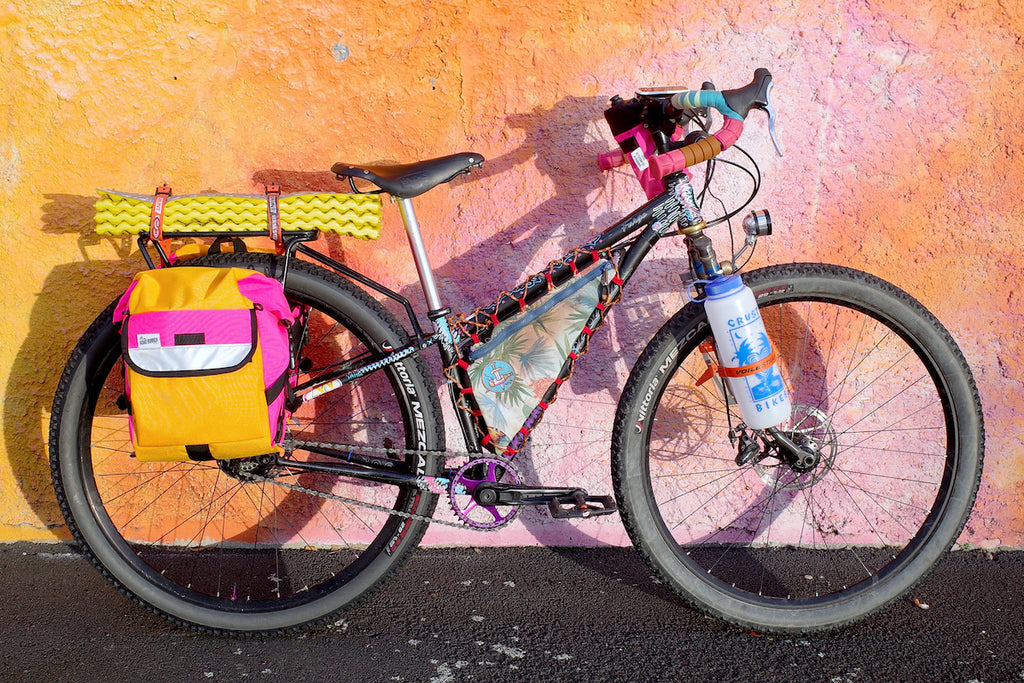 Off road mountain bicycle against bright color texture wall with Road Runner Bike Bags Anywhere Bikepacking Panniers mounted to rear rack with light shining on them